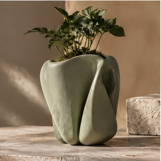 Sage-green sculptural ceramic planter with folded contours and foliage, without text overlay